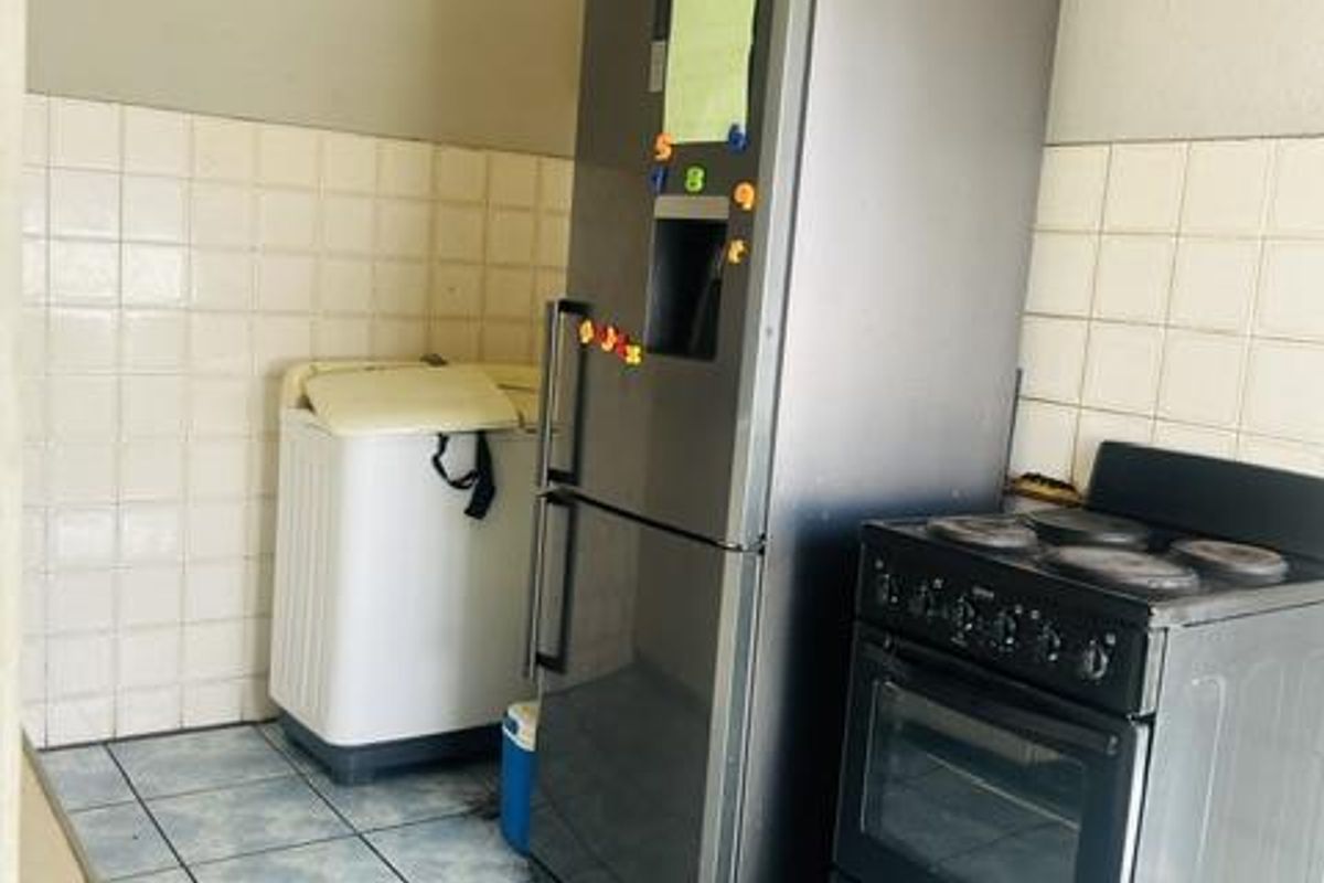 A functional kitchen area featuring tiled flooring, a tiled splashback, and a freestanding oven, requiring cosmetic updates to improve the overall finish.