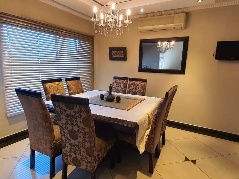 A well-maintained dining room featuring tiled flooring, a decorative chandelier, and a wall-mounted air conditioning unit.