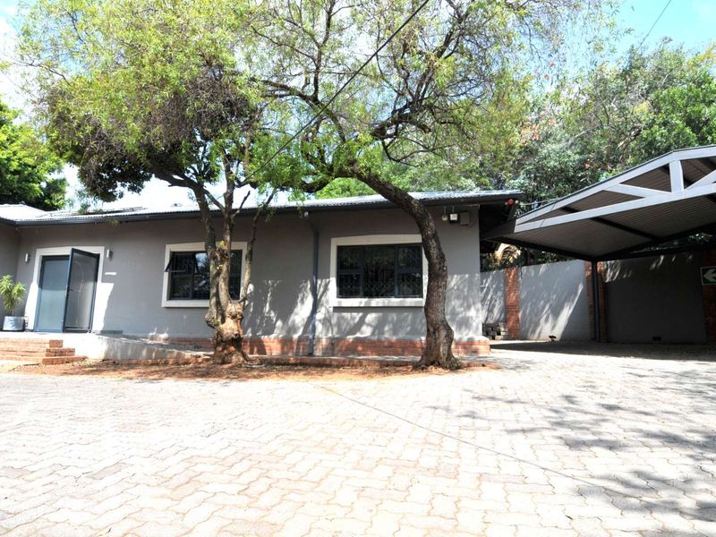 Front exterior view of the property featuring a paved driveway, covered carport, and established trees with a grey painted facade.