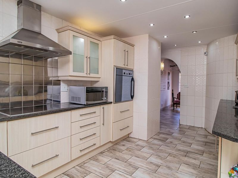 A well-maintained kitchen featuring light wood cabinetry, granite countertops, stainless steel appliances, and modern tiled flooring with recessed lighting.