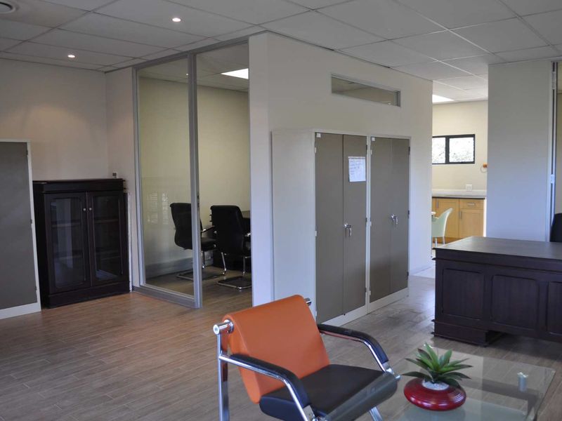 A professional office space featuring a glass-partitioned meeting room, built-in storage lockers, suspended ceilings with recessed lighting, and durable tiled flooring.