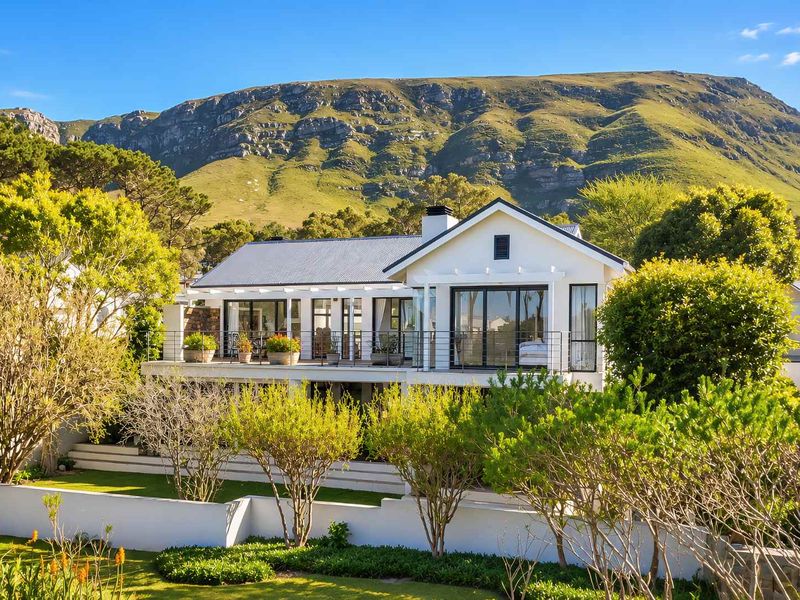 A beautiful rear view of the house featuring a spacious balcony, large sliding glass doors, and a well-maintained garden set against a mountain backdrop.