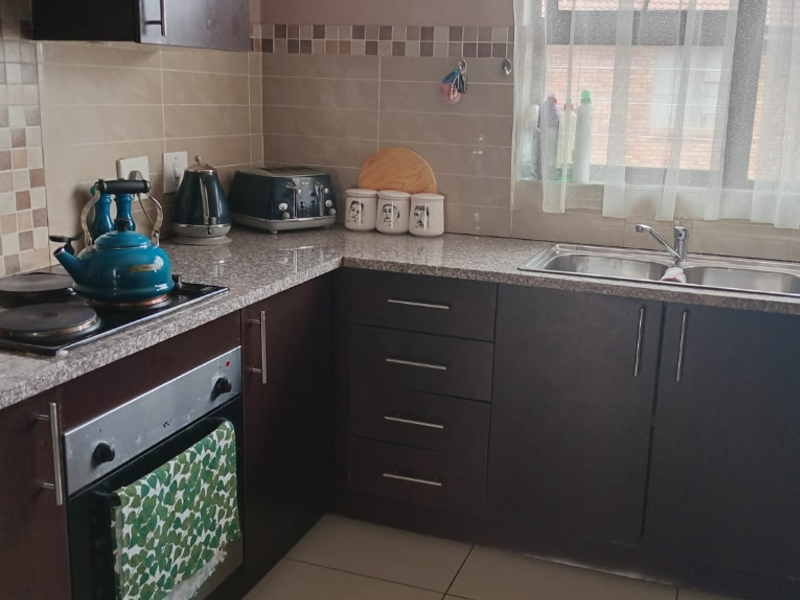 A functional kitchen featuring dark wood cabinetry, granite countertops, a built-in oven, electric hob, and a double bowl sink with tiled backsplash.