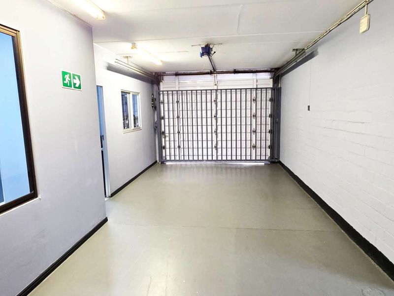 A clean, functional industrial garage space featuring a secure metal gate, painted concrete flooring, and integrated fluorescent lighting.