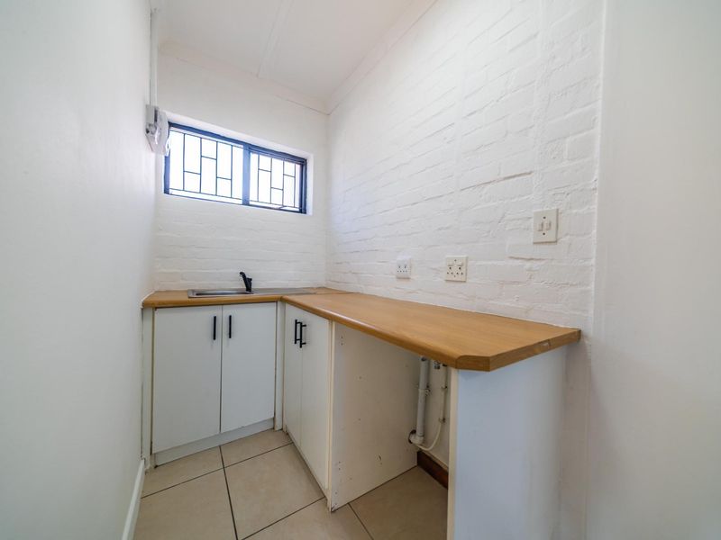 A functional laundry area featuring built-in cabinetry, a wooden countertop, a stainless steel sink, and tiled flooring with exposed brick wall detailing.