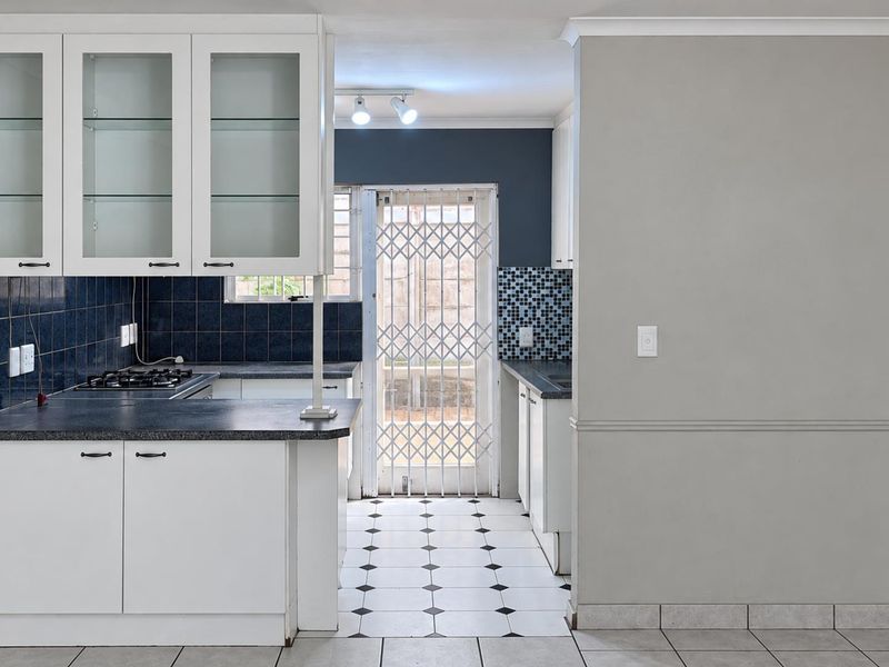 A functional kitchen featuring white cabinetry, a gas hob, dark tiled backsplash, and direct access to the exterior via a security gate.