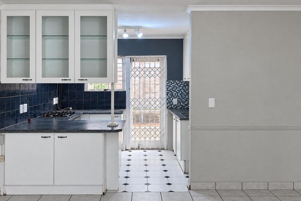 A functional kitchen featuring white cabinetry, a gas hob, dark tiled backsplash, and direct access to the exterior via a security gate.