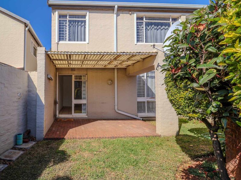 Rear view of the townhouse featuring a brick-paved patio area, covered by a corrugated roof, adjacent to a small private garden and boundary wall.
