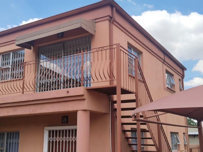 Rear exterior view of the cottage featuring a balcony with an external staircase, security fixtures, and a shade sail over the outdoor area.