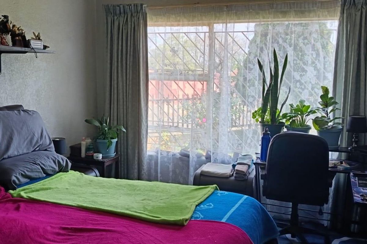 A functional bedroom featuring a large window with security bars and curtain rails, providing natural light and a view of the exterior.