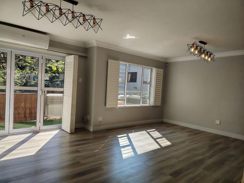 Spacious living area featuring modern laminate flooring, plantation shutters, split-system air conditioning, and stylish pendant lighting with direct access to an outdoor space.