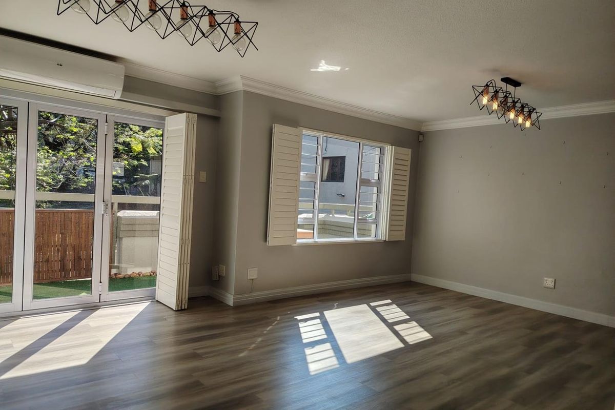 Spacious living area featuring modern laminate flooring, plantation shutters, split-system air conditioning, and stylish pendant lighting with direct access to an outdoor space.