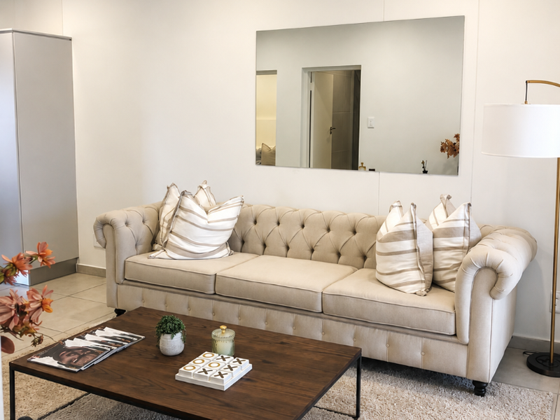 A well-lit living room featuring neutral tiled flooring, recessed ceiling lighting, and a large wall-mounted mirror, creating a bright and inviting atmosphere.