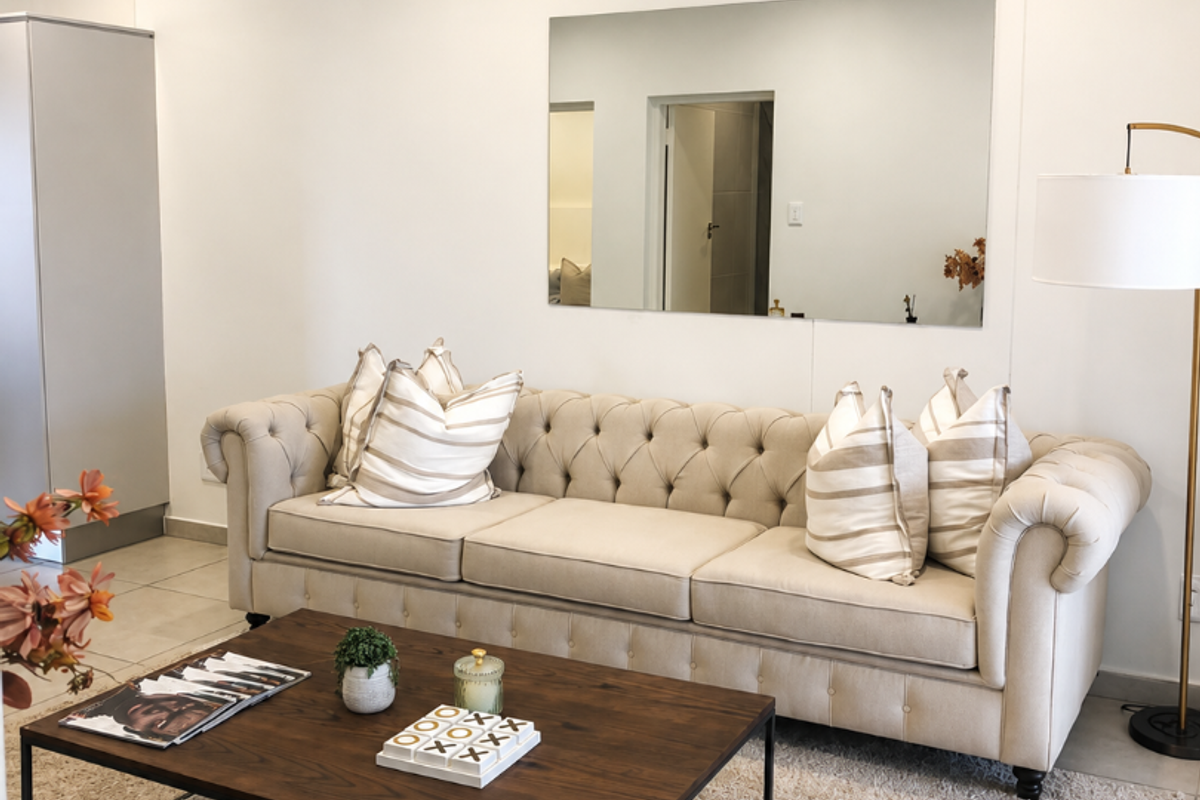 A well-lit living room featuring neutral tiled flooring, recessed ceiling lighting, and a large wall-mounted mirror, creating a bright and inviting atmosphere.