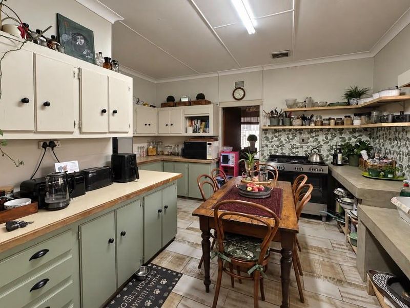 A rustic-style kitchen featuring concrete countertops, double basin sink, gas stove, and ample built-in cabinetry with a tiled backsplash and flooring.