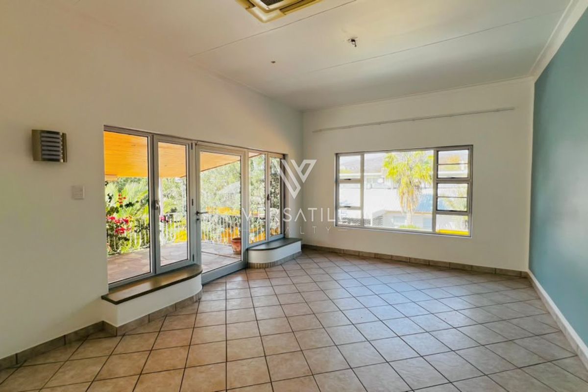 Spacious, empty living area featuring tiled flooring, large aluminium windows, and sliding glass doors leading to an outdoor patio space.