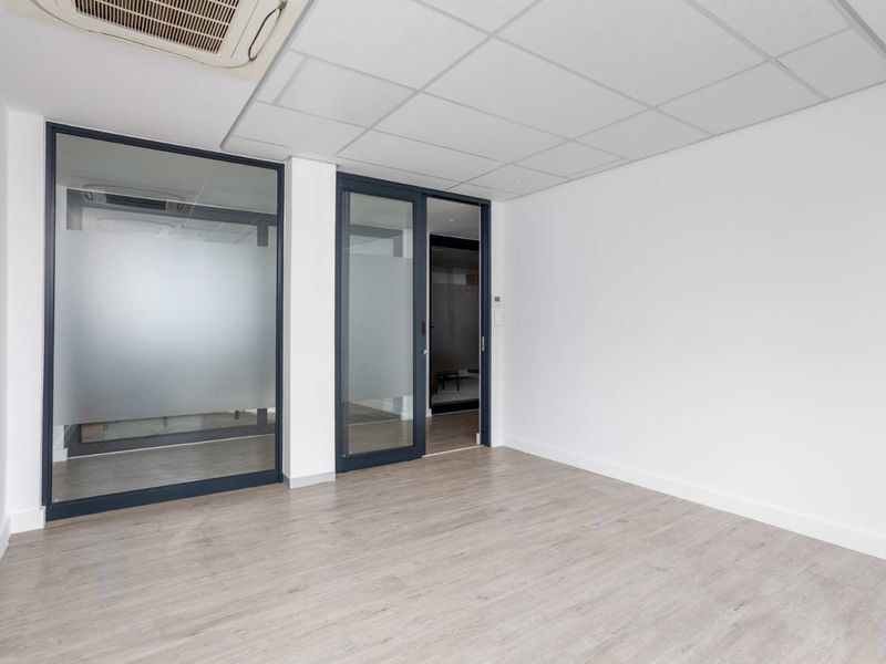 A bright, modern office space featuring laminate flooring, a suspended ceiling with integrated air conditioning, and glass partition walls for a professional, open feel.