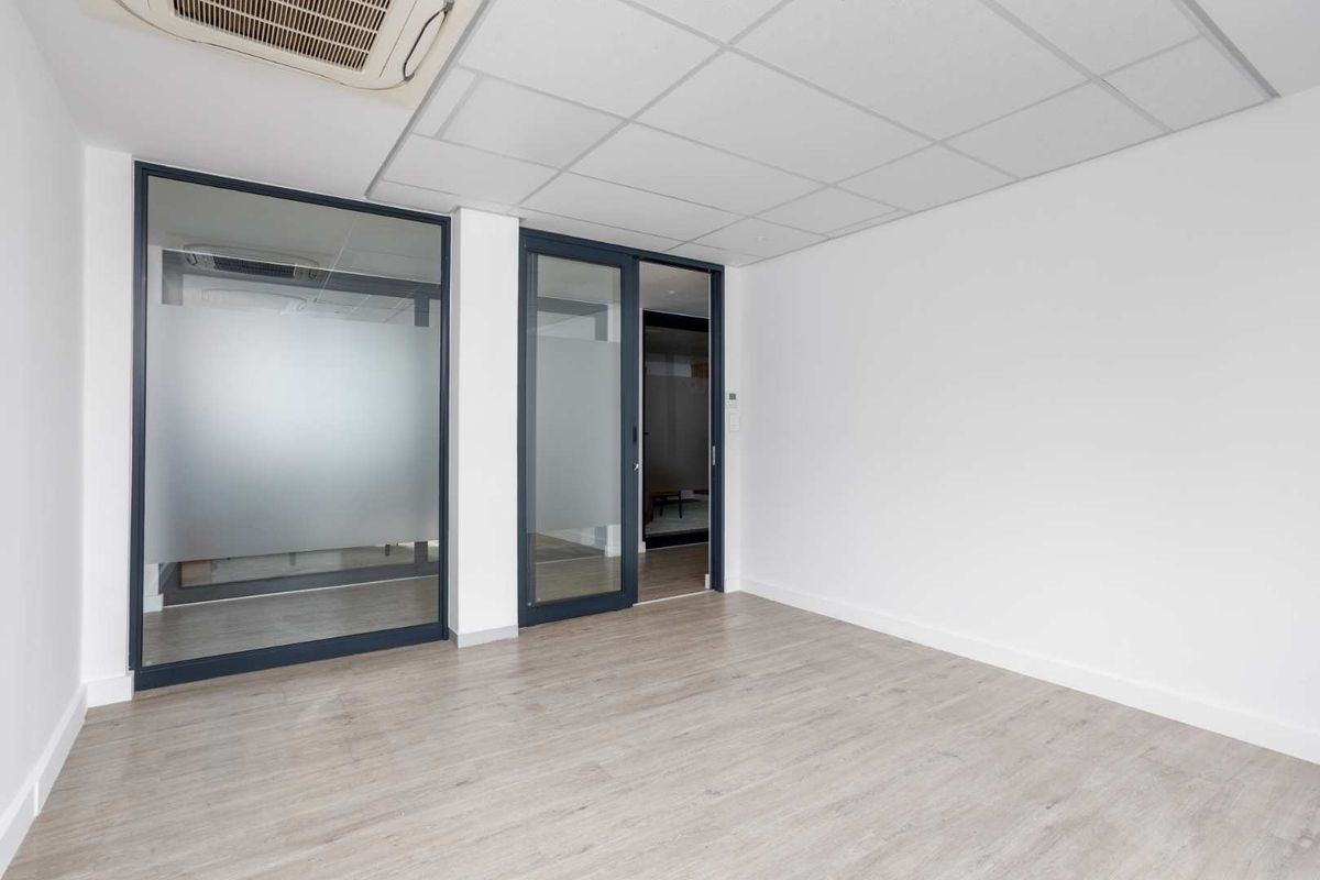 A bright, modern office space featuring laminate flooring, a suspended ceiling with integrated air conditioning, and glass partition walls for a professional, open feel.