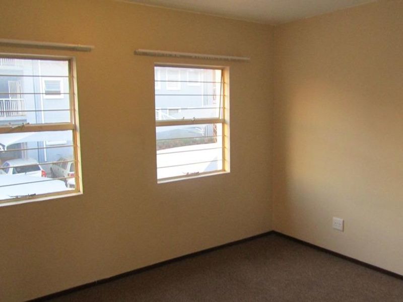 An empty bedroom featuring neutral walls, carpeted flooring, and windows fitted with security bars.