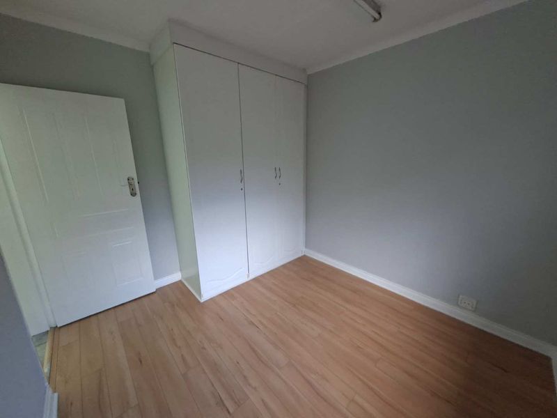A clean, empty bedroom featuring light-toned laminate flooring, neutral grey walls, and a white built-in wardrobe.