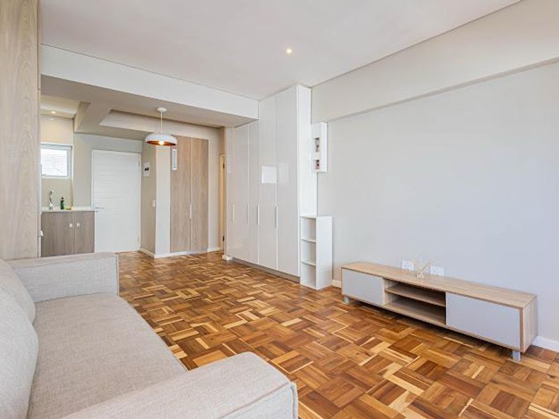 Open plan living area featuring warm parquet flooring, extensive built-in white cabinetry, and a compact kitchenette area with neutral finishes.