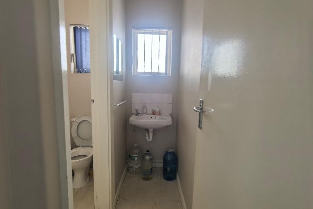 A compact bathroom featuring a wall-mounted basin, a toilet, and security bars on the window, with neutral wall finishes.