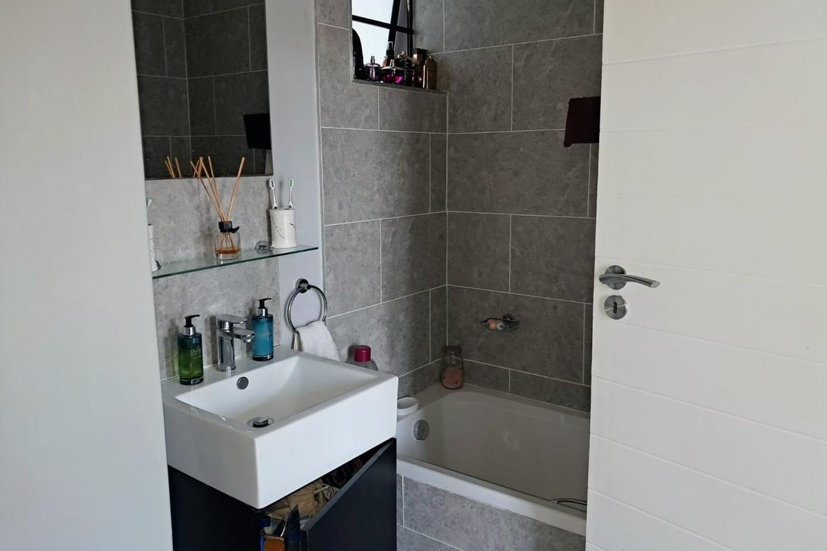 A compact bathroom featuring grey wall tiles, a built-in bathtub, and a modern vanity basin with a wall-mounted mirror.