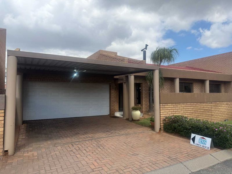 Front elevation of a brick cluster home featuring a paved driveway, covered carport, and a single garage door.