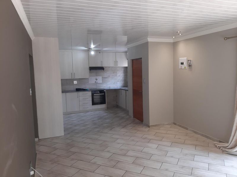 An open-plan living and kitchen area featuring modern tiled flooring, neutral wall tones, built-in cabinetry, and integrated kitchen appliances.