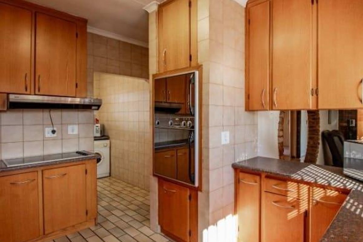 A functional kitchen featuring wooden cabinetry, tiled flooring, a built-in oven, and a tiled backsplash, offering a traditional layout with a separate scullery area.