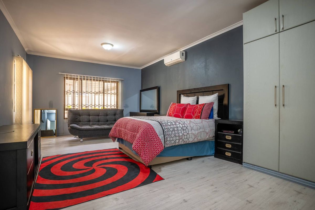 Spacious bedroom featuring light-toned laminate flooring, built-in cabinetry, and a wall-mounted air conditioning unit.