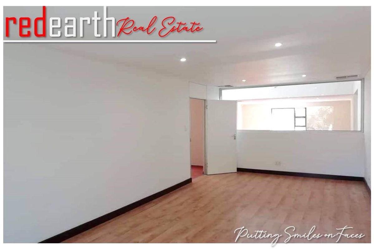 A bright, empty living area featuring wood-look laminate flooring, recessed ceiling lighting, and a large horizontal window providing natural light.