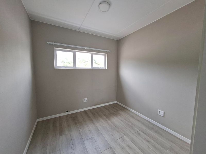 A clean, empty bedroom featuring neutral wall paint, modern laminate flooring, and a window providing natural light.
