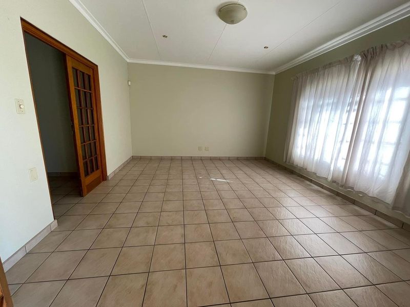 A spacious, empty living room featuring neutral ceramic floor tiles, a wooden french door, and simple ceiling finishes, ready for personalization.