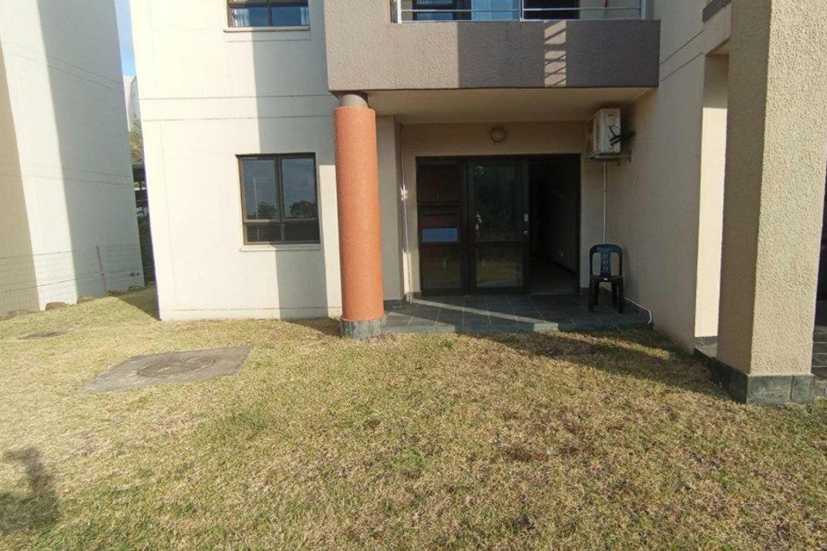 Rear view of the apartment featuring a small tiled patio area, sliding glass doors, and a private lawn space.