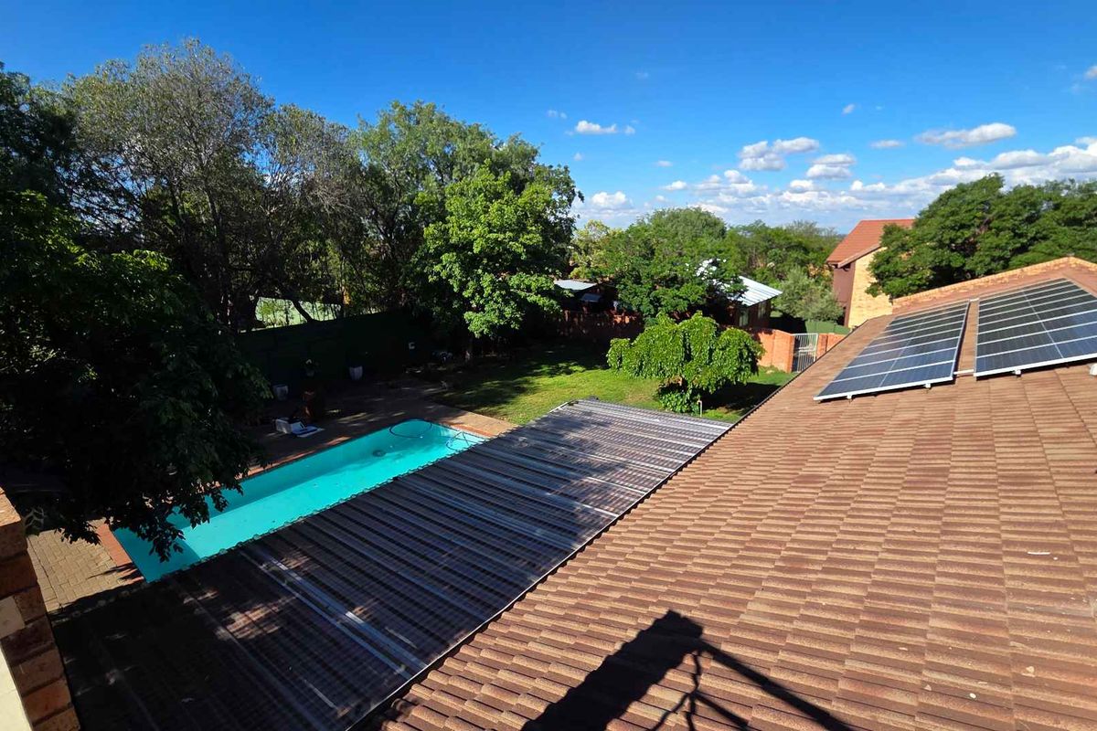 Elevated view of the property featuring a tiled roof with solar panels, a swimming pool, and a spacious garden area.
