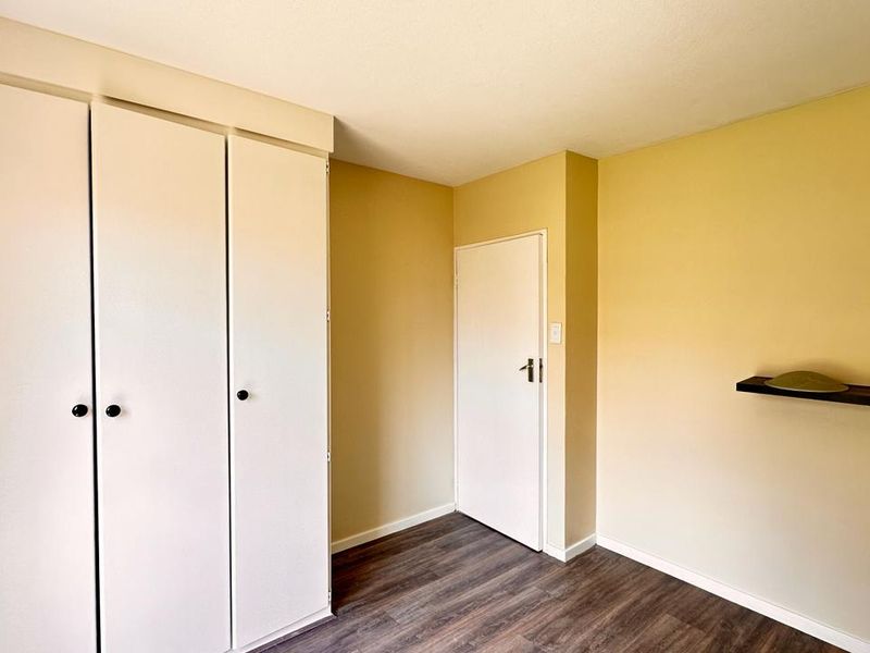 A clean, empty bedroom featuring built-in cupboards, laminate flooring, and neutral wall paint, offering a blank canvas for personalization.