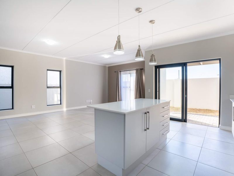 Modern open-plan living area featuring a central kitchen island with quartz countertops, tiled flooring, and sliding doors leading to the outdoor space.