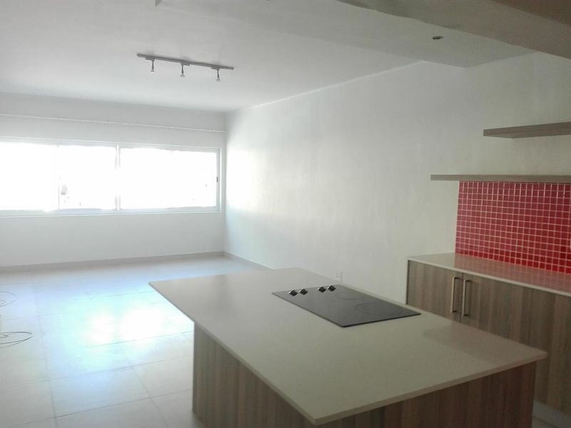 Spacious open-plan living and kitchen area featuring a central island with a built-in cooktop, modern cabinetry, and bright, neutral finishes.