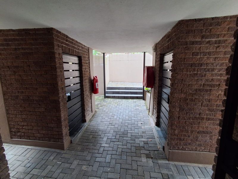 A covered outdoor walkway featuring brick masonry walls and paved flooring, leading to a set of concrete steps.