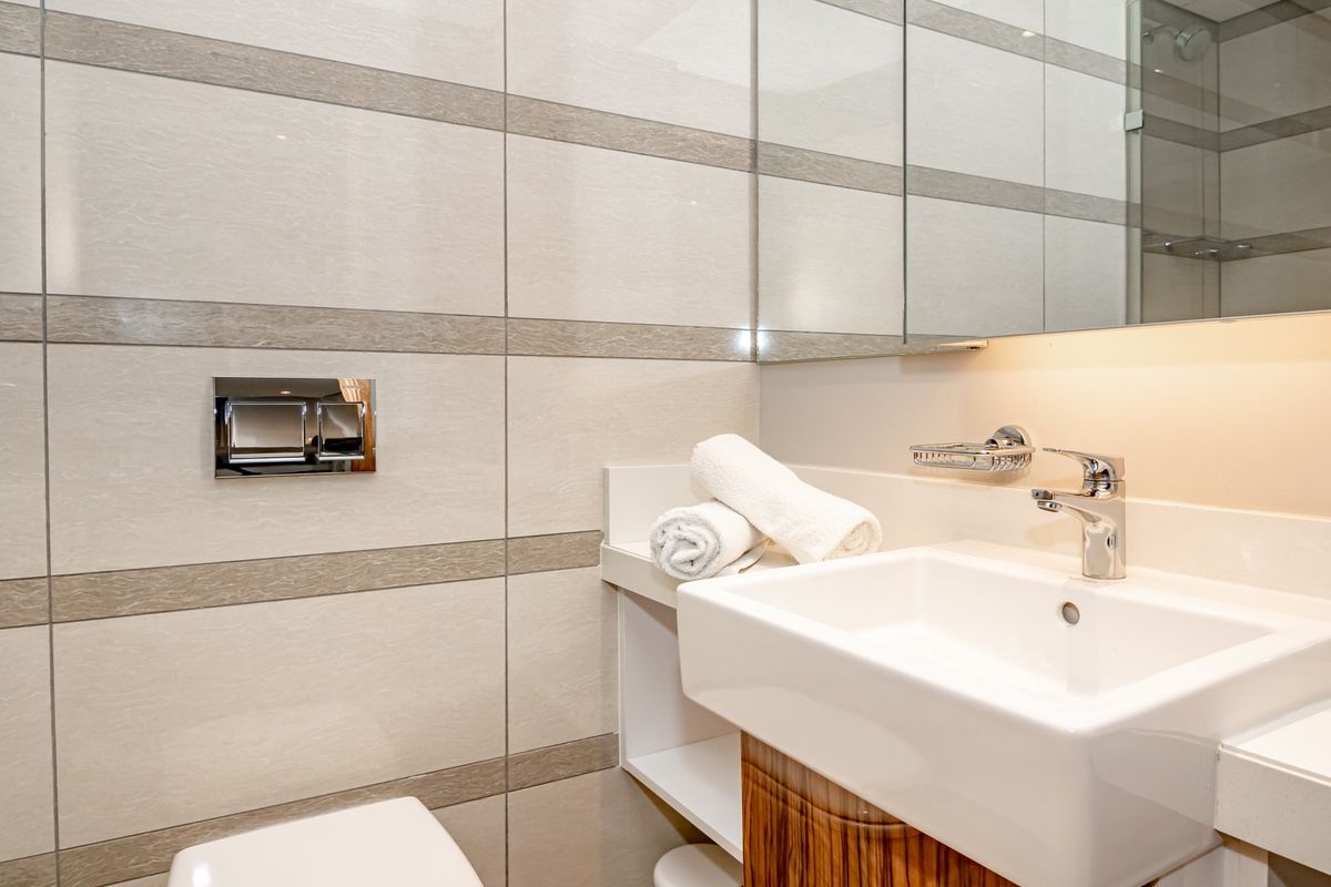 Modern bathroom featuring a wall-mounted toilet, sleek vanity with integrated basin, and large wall-mounted mirror with under-cabinet lighting.