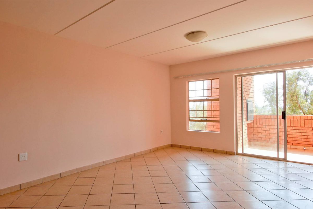 A bright, empty living room featuring tiled flooring, a large window, and a sliding glass door providing access to an outdoor balcony area.