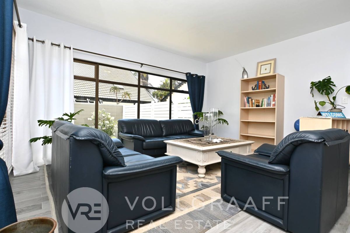 A bright living room featuring large windows that provide natural light and a view of the exterior, finished with modern wood-look flooring.