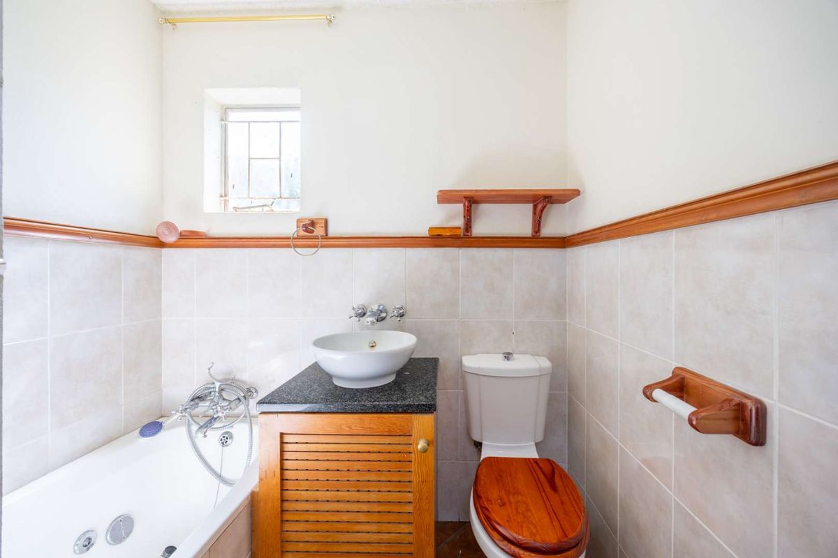 A functional bathroom featuring a bathtub, vessel sink with granite vanity, and wooden accents, offering a dated aesthetic ready for modernization.