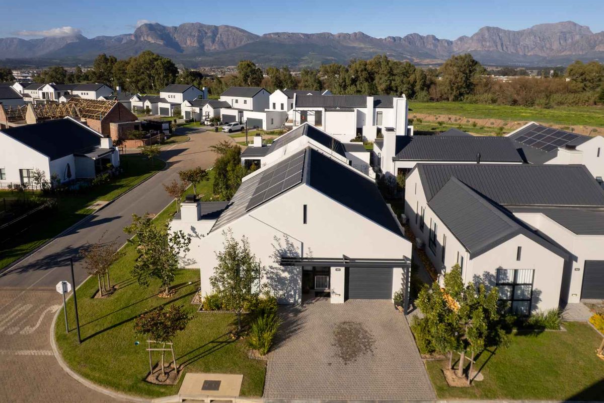Aerial view of a modern residential property featuring a paved driveway, garage, and solar panels, situated in a well-maintained estate with mountain views.