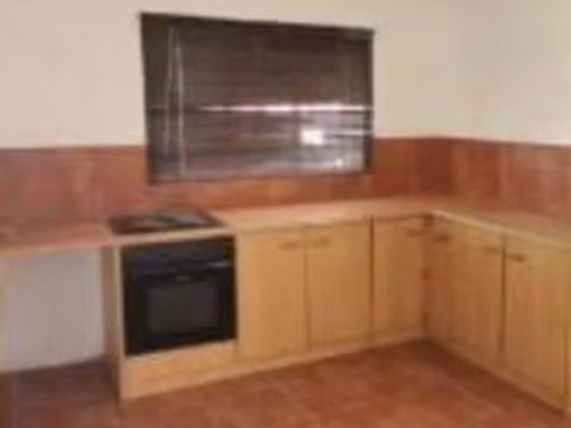 A functional kitchen featuring wooden cabinetry, a built-in oven, hob, and tiled finishes throughout.