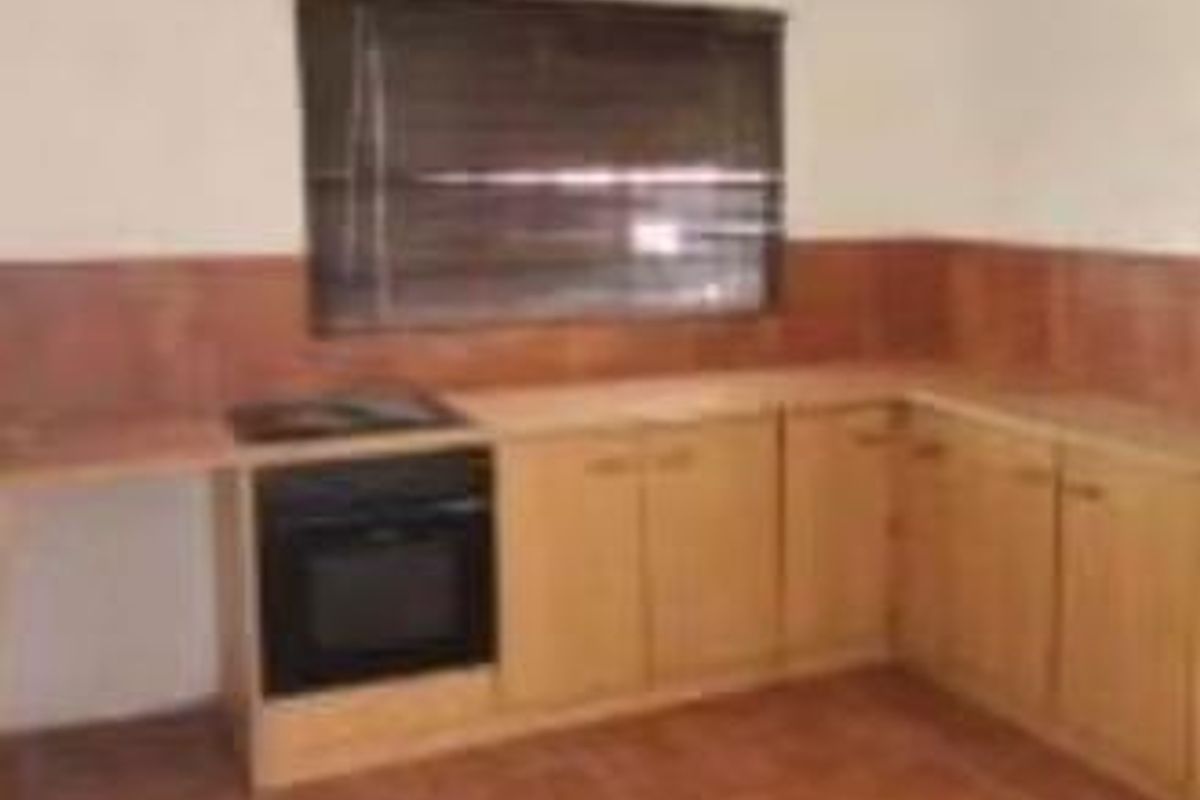 A functional kitchen featuring wooden cabinetry, a built-in oven, hob, and tiled finishes throughout.
