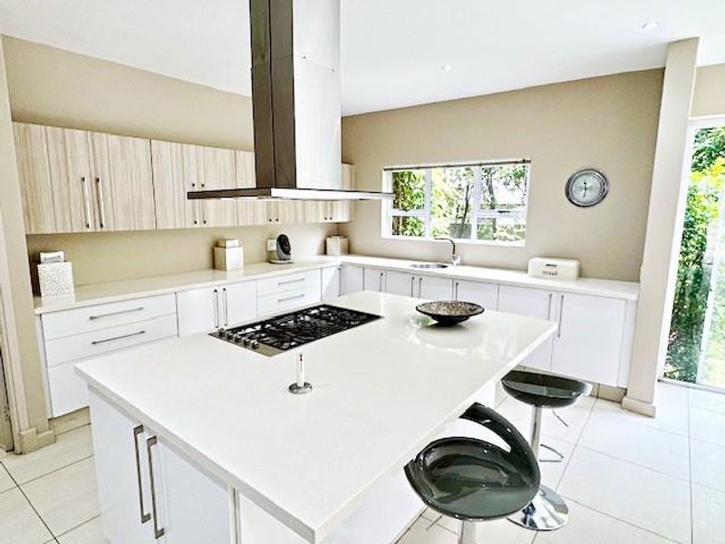 Modern kitchen featuring a central island with a gas hob, stainless steel extractor fan, ample built-in cabinetry, and stone countertops with tiled flooring.