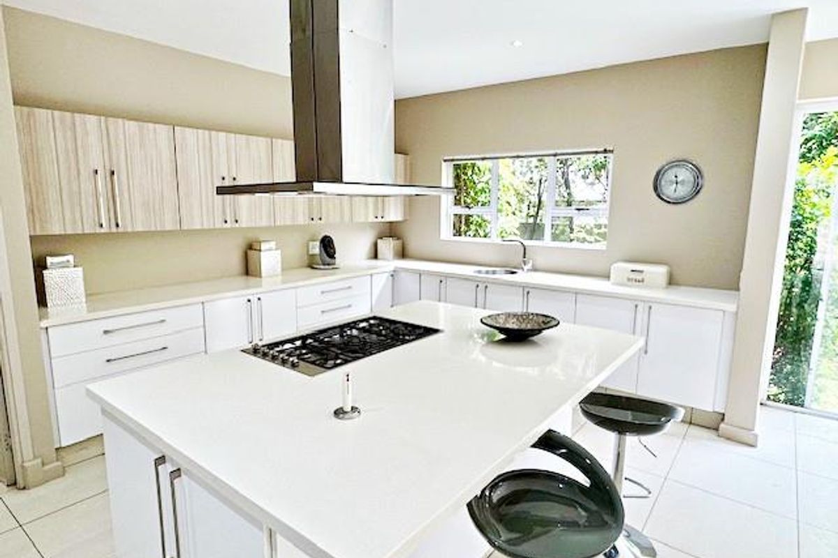 Modern kitchen featuring a central island with a gas hob, stainless steel extractor fan, ample built-in cabinetry, and stone countertops with tiled flooring.