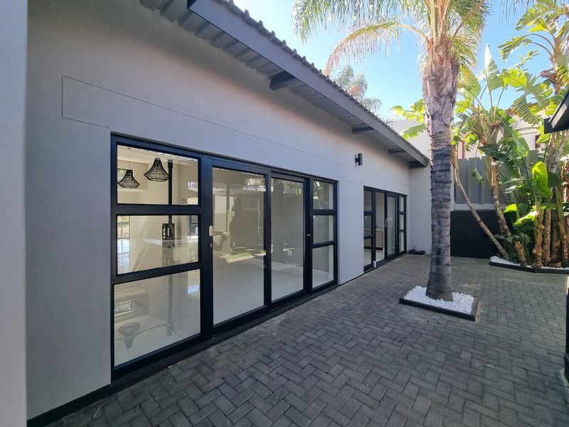A modern rear exterior view featuring a paved patio area, black aluminium sliding doors, and well-maintained exterior finishes.